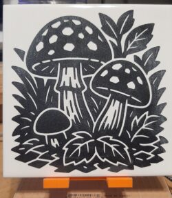 A laser-engraved ceramic tile featuring bold mushroom cluster artwork, engraved from licensed design.
