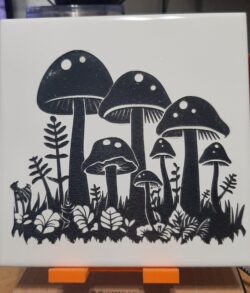 A laser-engraved ceramic tile featuring a mushroom grove illustration, engraved from licensed design.