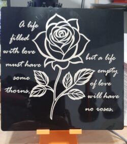 A laser-engraved black acrylic plaque featuring a rose illustration and a poetic quote — engraved with an IR laser for a subtle gold-tinted finish.